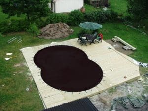 Ett bakgårdsdäck med en täckt oval pool med POOLSKYDD SVART 3,6 X 6,6 M och utemöbler under ett paraply.