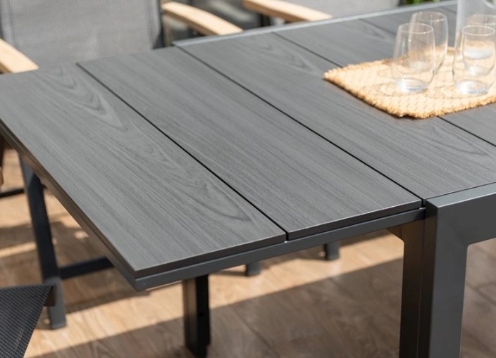 Närbild av BORD ESSENCE ALU 156-246 x 95 cm grått bord med fyra tomma glas på en matta.