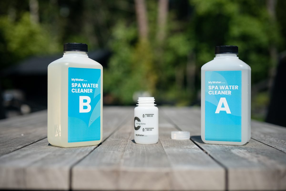 Två MYWATER SPA WATER CLEANER-flaskor bredvid en liten öppen behållare på bordet.