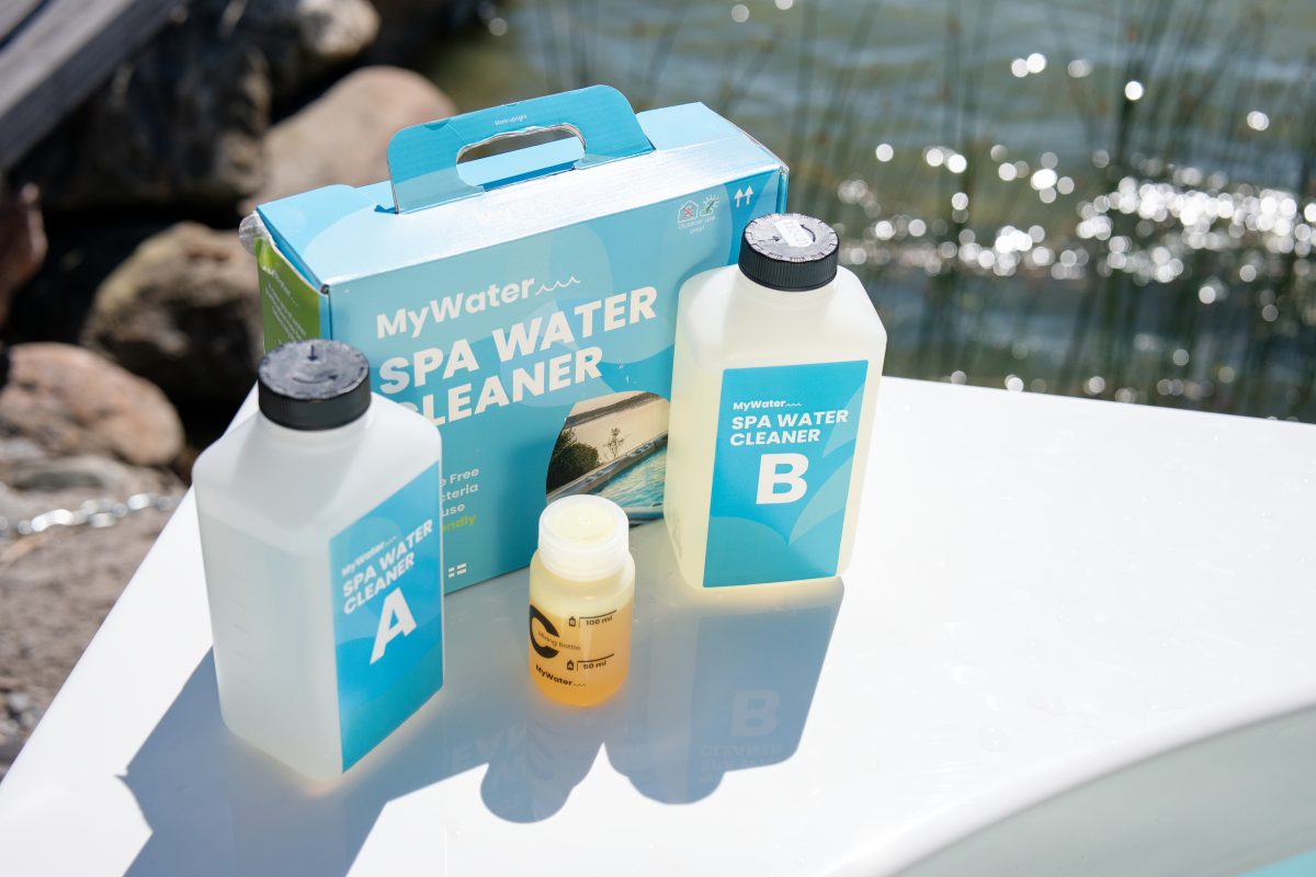 Tre flaskor och en förpackning med MYWATER SPA WATER CLEANER bredvid en vattenyta utomhus.